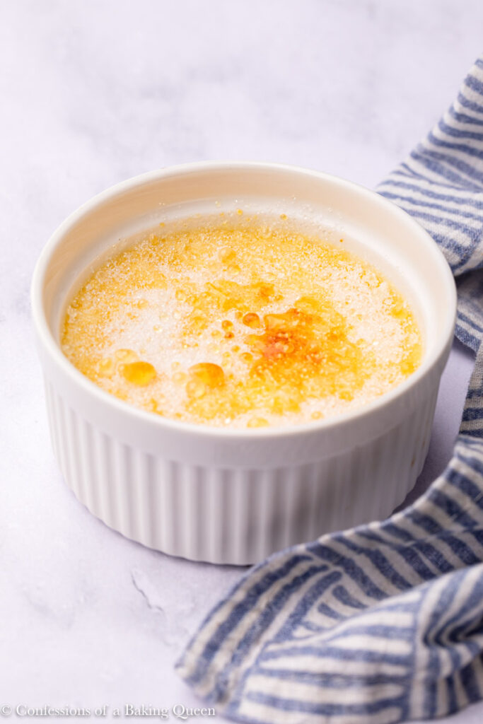 burning the sugar on top of lemon creme brûlée on a white surface with a blue linen