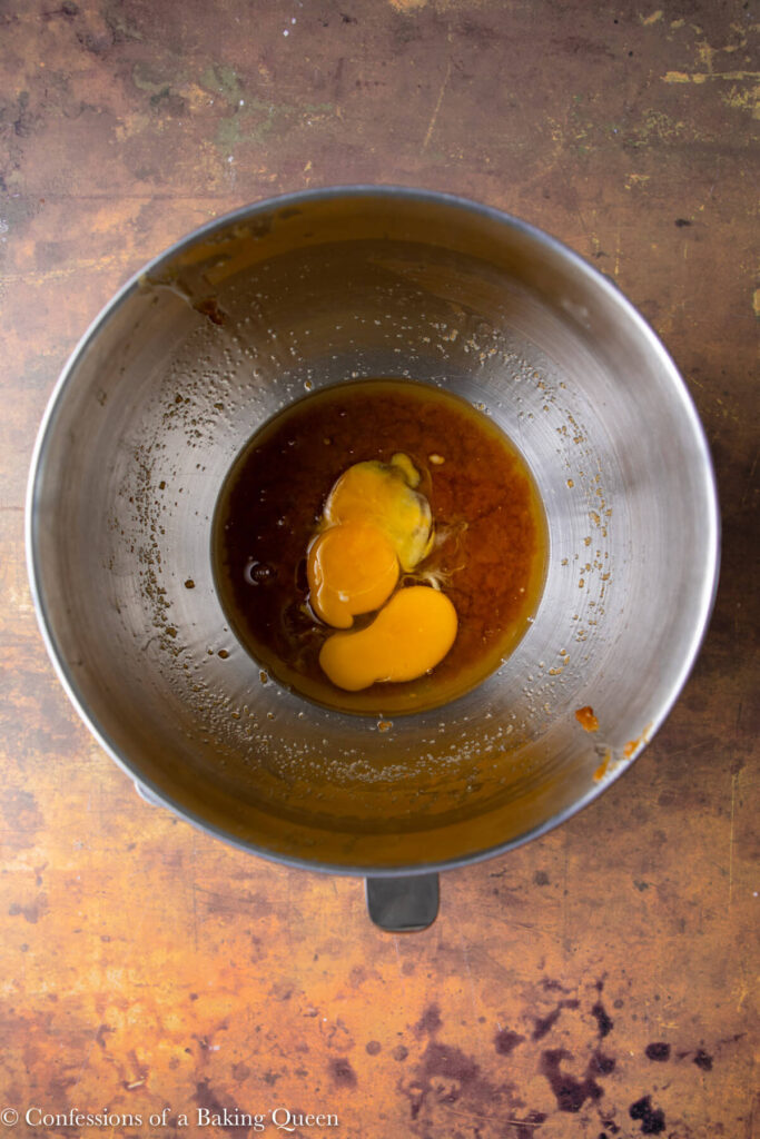egg and egg yolk added to butter and sugar mixture in a mixing bowl on a brown and orange distressed surface