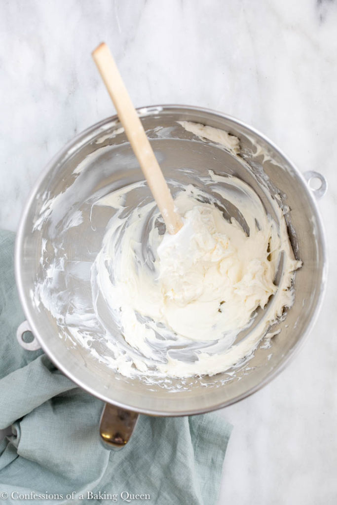cream cheese beaten in a metal bowl with a white spatula