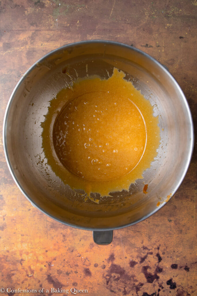 wet ingredients mixed together in a metal bowl for chocolate chip cookie dough in a metal mixing bowl on an orange and brown distressed surface