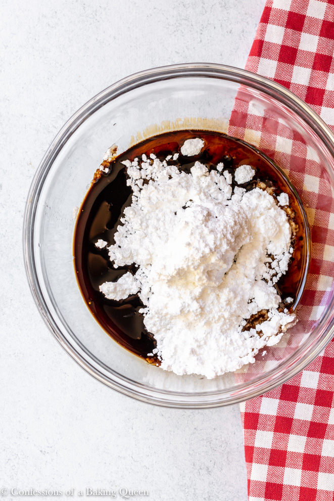powdered sugar and maple syrup in a glass bowl on a white counter next to a red linen