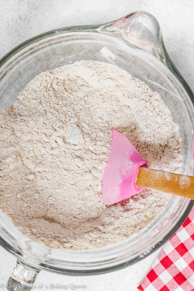 dry ingredients mixed together in a glass bowl with a pink spatula on a white counter next to a red linen