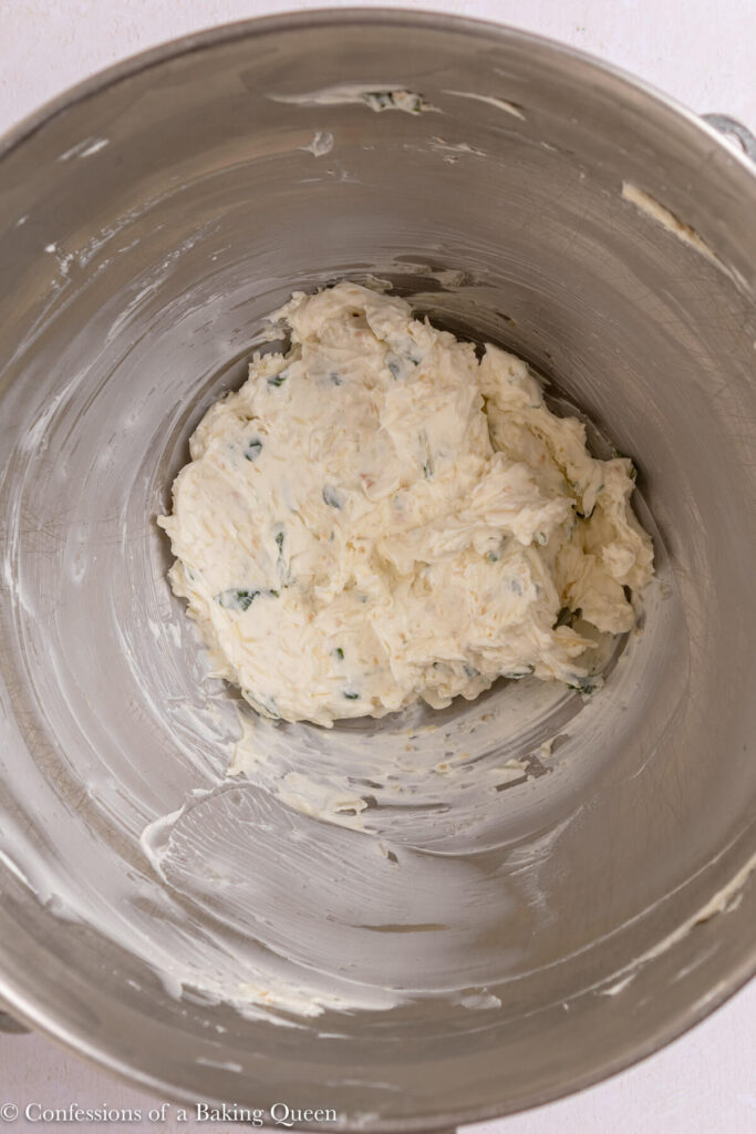 cheesey cream cheese mixture in a metal mixing bowl on a light pink surface