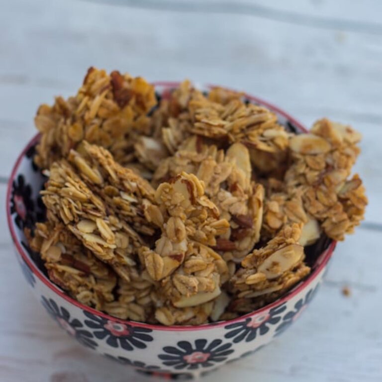 Maple Almond Granola Clusters baked and served in a white, black and pink bowl on a white background
