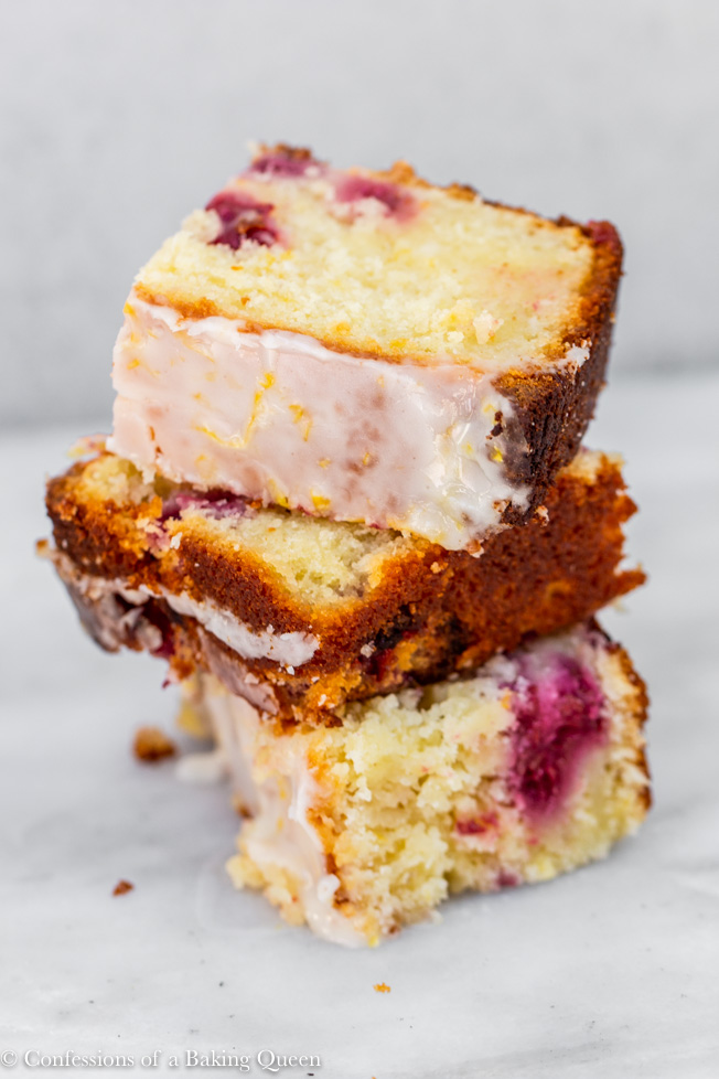 close up of raspberry lemon loaf cake pieces stacked on top of each other on a white marble surface