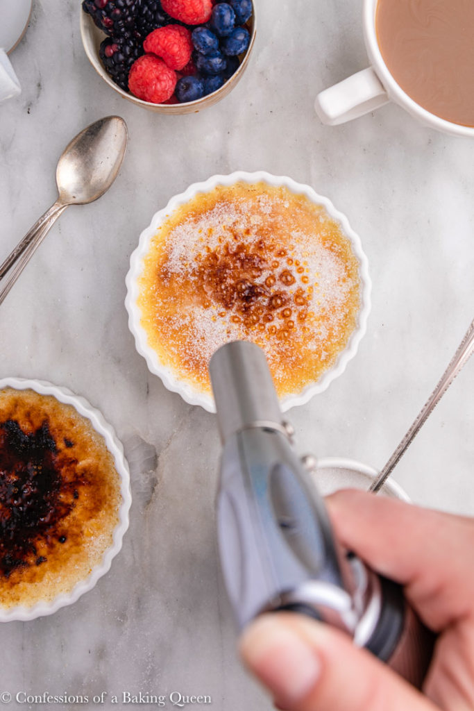 hand holding a kitchen torch torching creme brulees