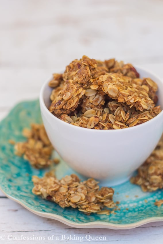 Cookie Butter Granola in a white cup on a blue plate overflowing on top of a white background