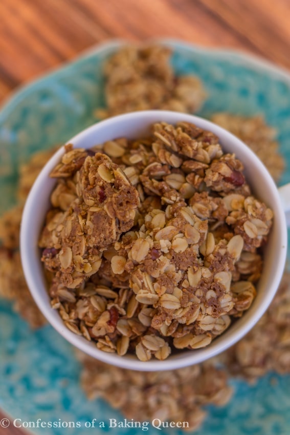 Cookie Butter Granola in a white cup on a blue plate from overhead  on a wood background