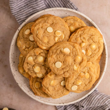 plate of white chocolate chip cookies on a round white plate on a light brown surface with a blue linen