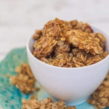 Cookie Butter Granola in a white cup on a blue plate overflowing on top of a white background