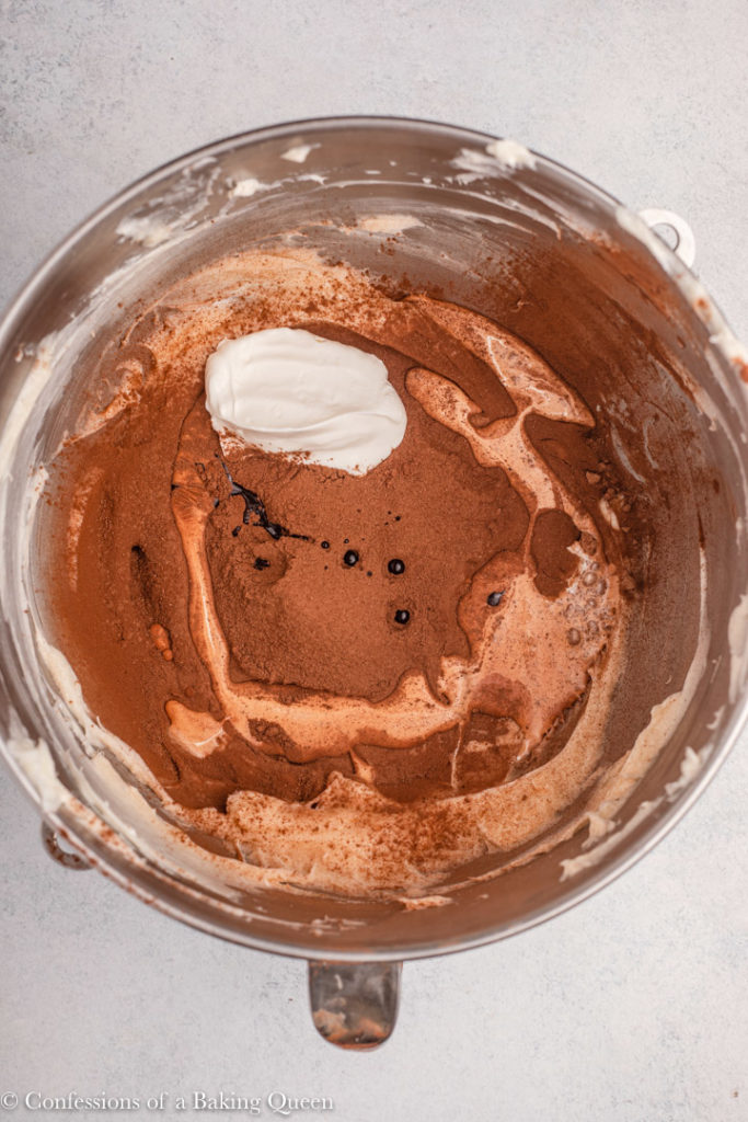 cocoa powder, sour cream, vanilla, and heavy cream in a large metal bowl on a light grey background 