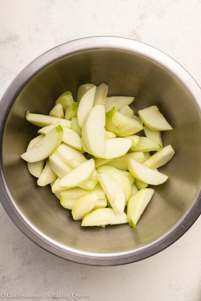 bowl full of peeled and sliced granny smith apples on a white background