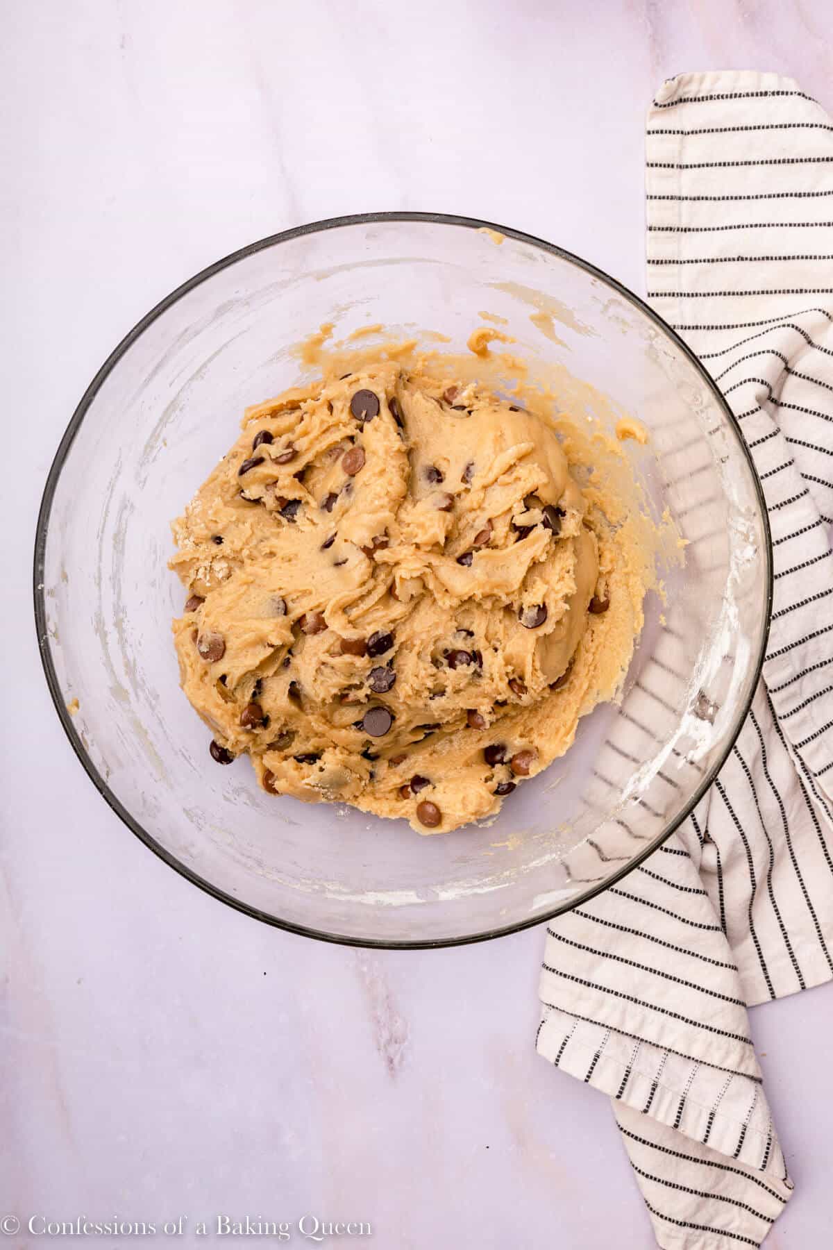chocolate chip cookie dough in an glass bowl on a marble surface with a white stripped linen