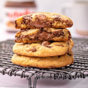 stack of nutella chocolate chip cookies on a black wire rack on a light pink surface