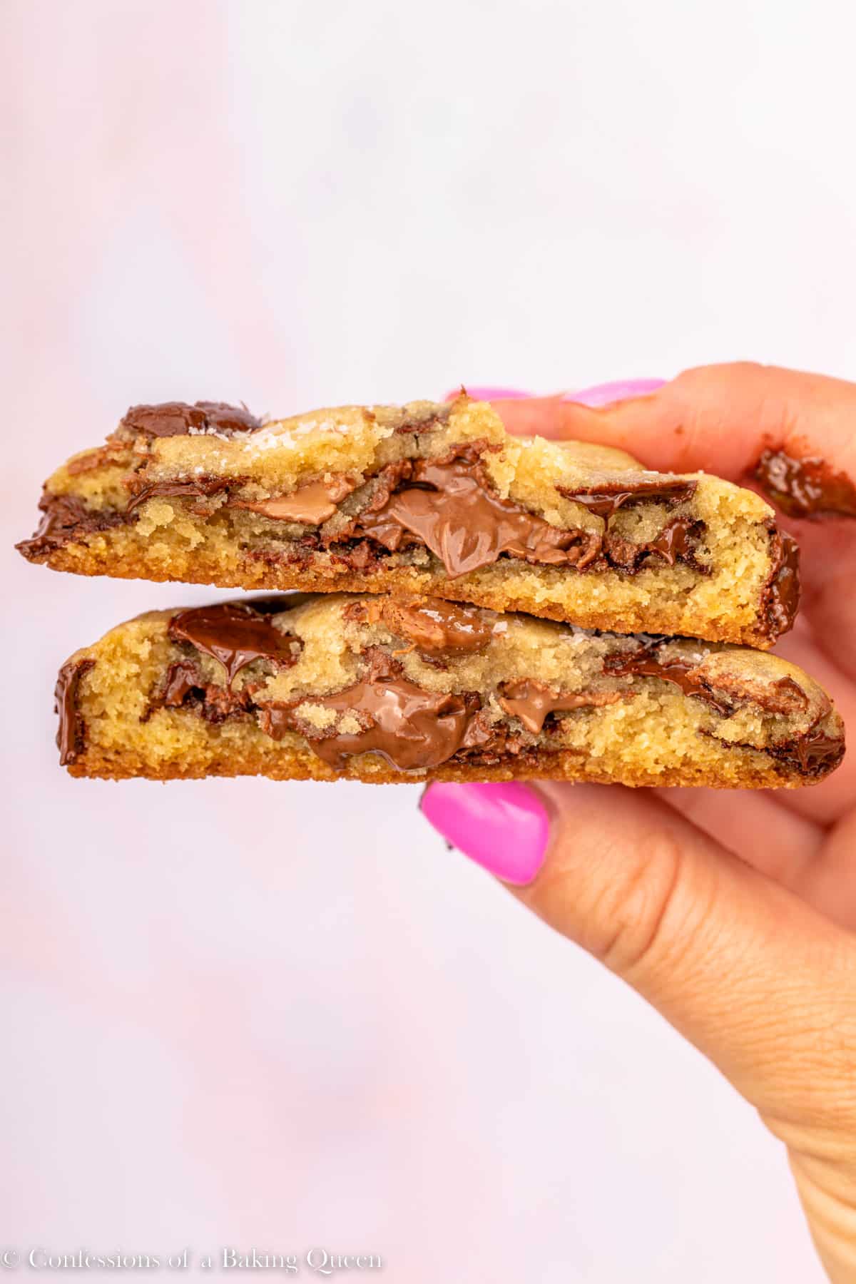 hand holding a broken in half nutella stuffed chocolate chip cookie over a pink surface