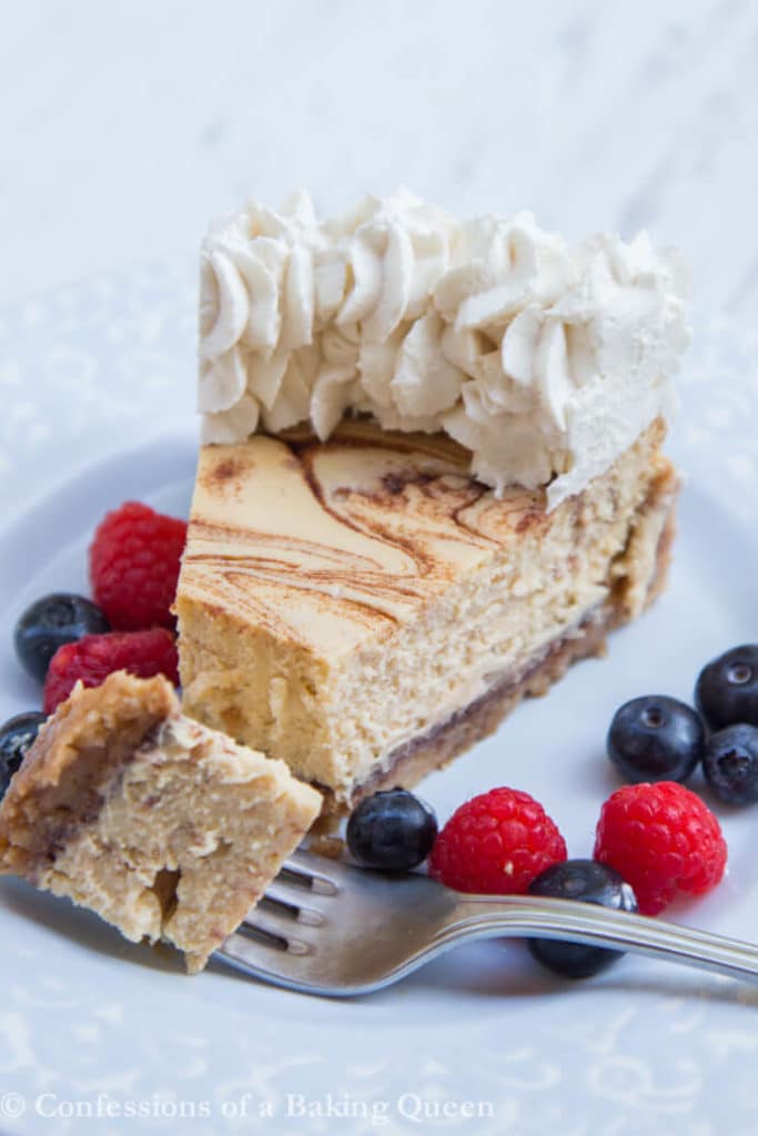 Cinnamon Roll Cheesecake on a light blue plate with a fork taking a bite and lots of fresh berries on a white background