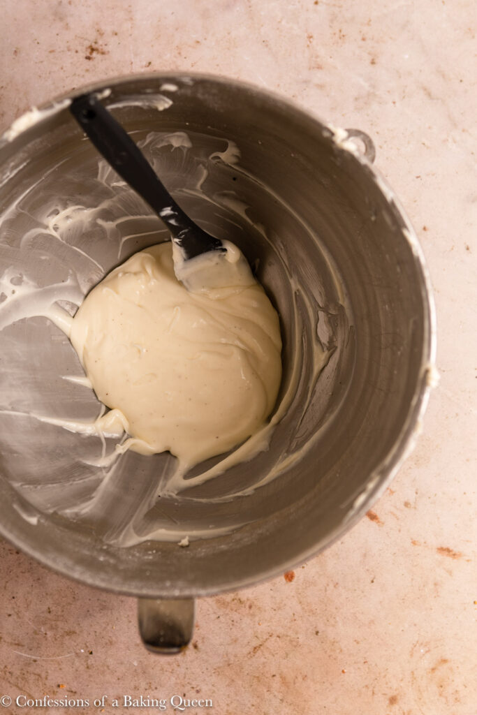 cream cheese frosting in a metal mixing bowl with a grey spatula on a light brown surface