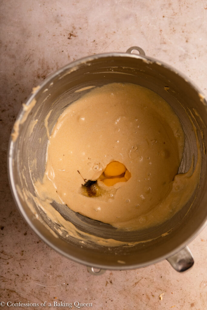 egg and vanilla added to sugar butter mixture in a metal mixing bowl on a light brown surface