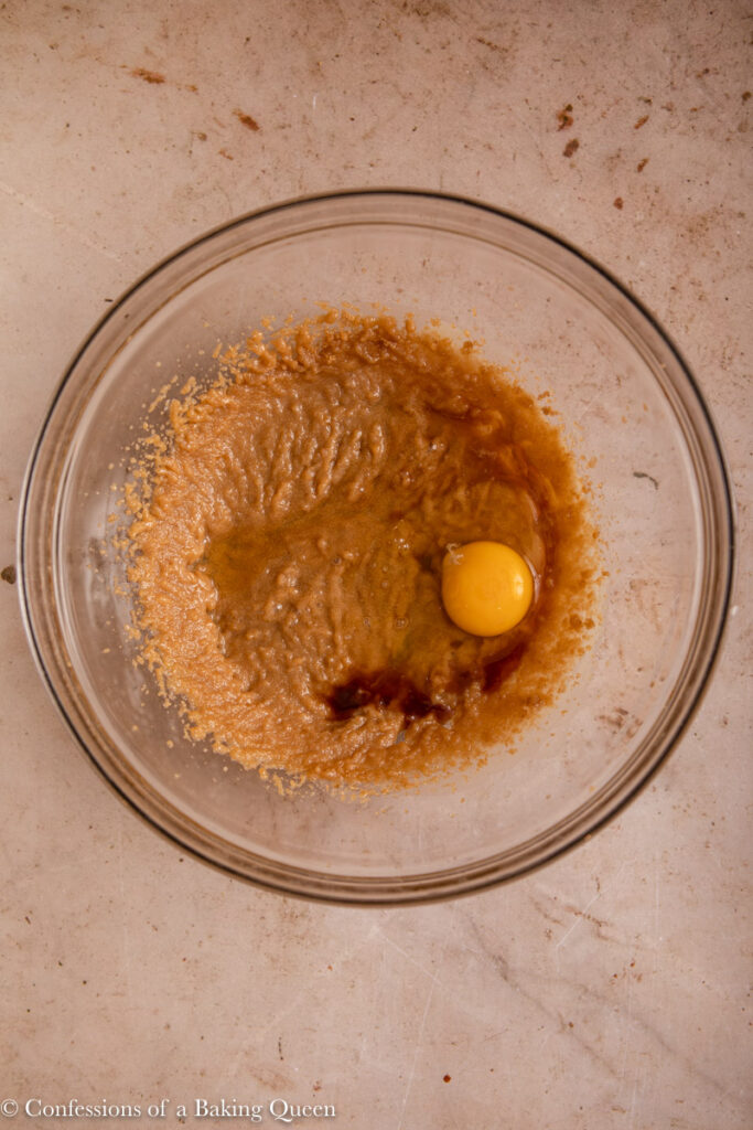 egg and vanilla added to creamed butter and sugar in a glass bowl on a light brown surface