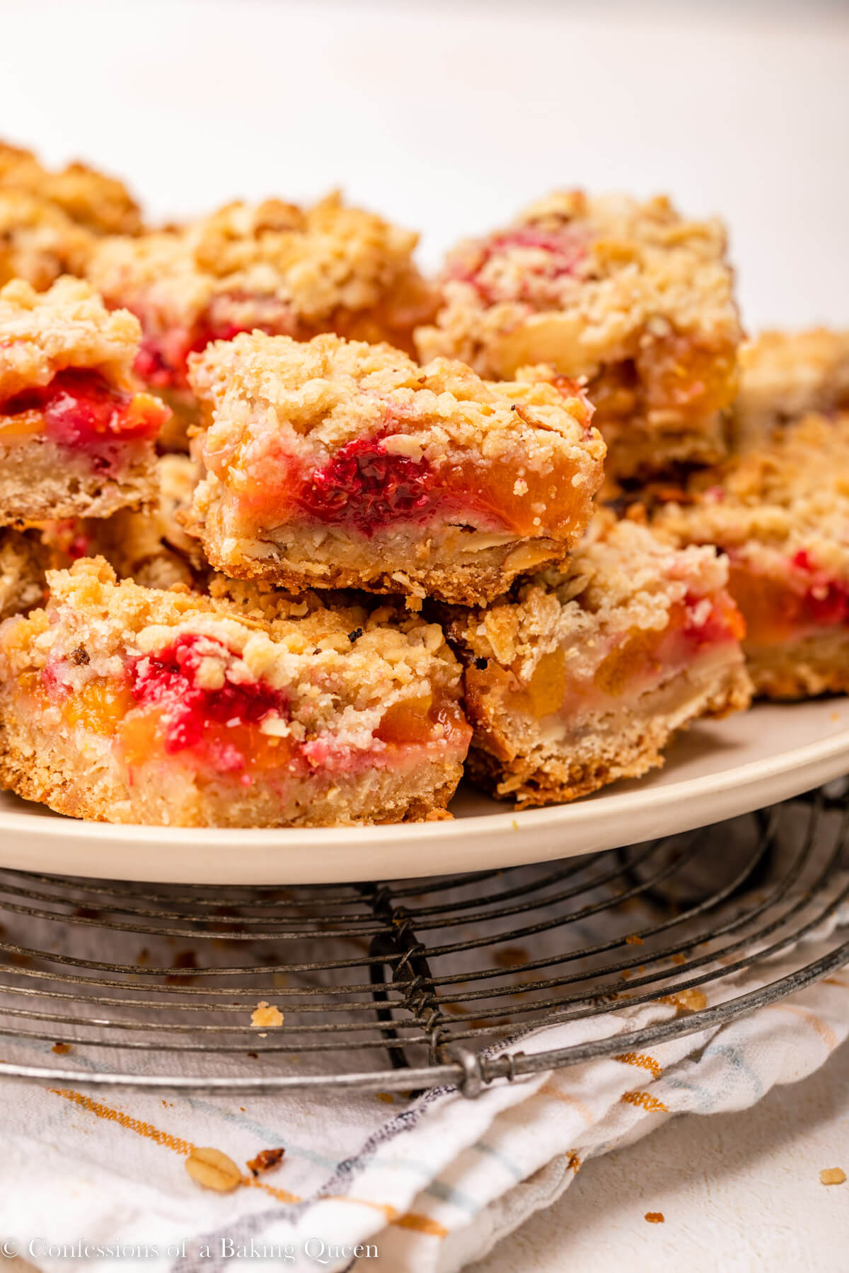 peach raspberry crumb bars on a tan plate on top of a stripped linen on a light surface