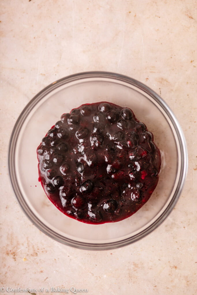 blueberry sauce cooling in a glass bowl on a light brown surface