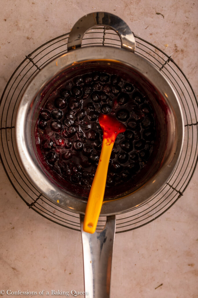 cooked blueberry sauce in a metal saucepan on top of a wire rack on a light brown surface