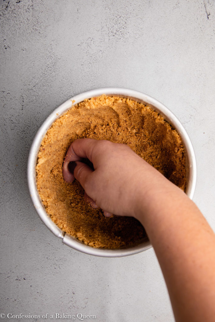 hand pressing graham cracker crust into pan
