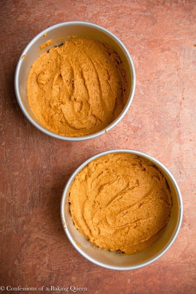 pumpkin cake batter in cake pans before baking sitting on a reddish brown surface