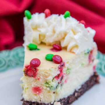 Brownie Bottom Cheesecake slice on a white plate with green rim and red towel in the background