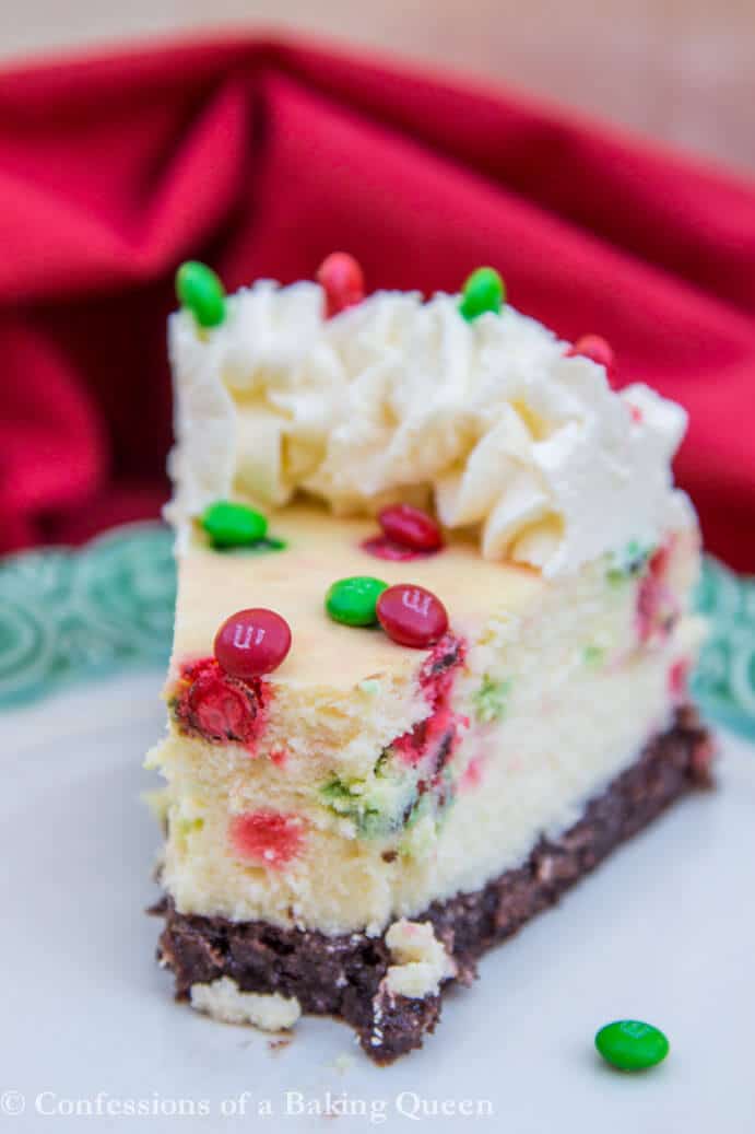 Brownie Bottom Cheesecake slice on a white plate with green rim and red towel in the background