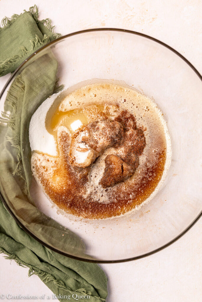 brown butter poured on top of white sugar and brown sugar in a glass bowl on an light pink surface with a dark green napkin