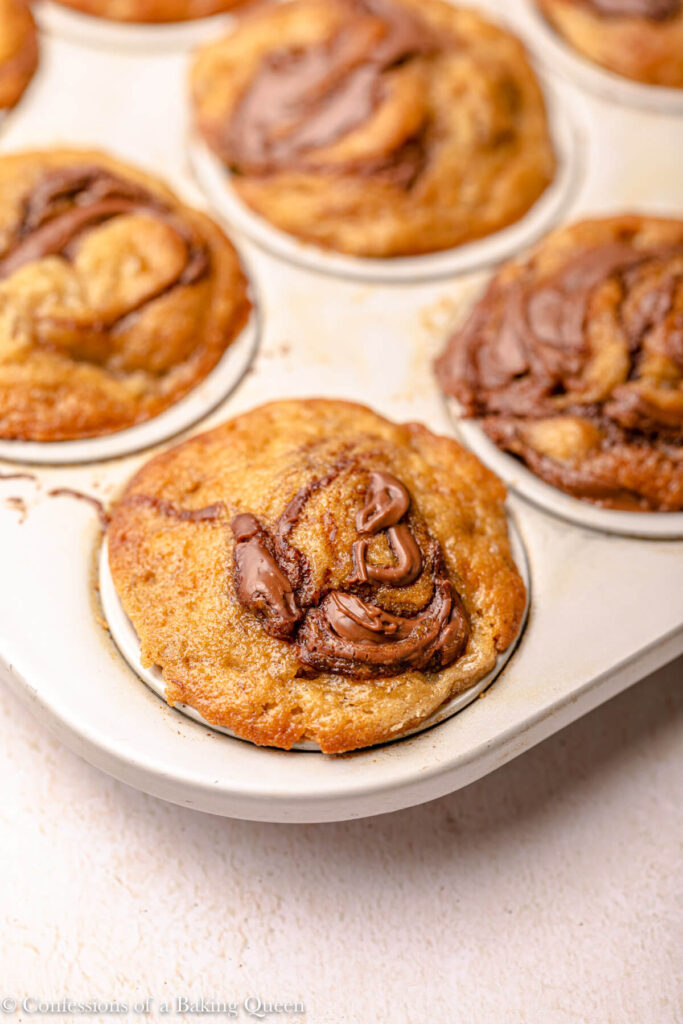 close up of nutella banana muffins in a baking tray on a light pink surface