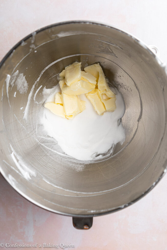 granulated sugar and butter in a metal mixing bowl on a light pink surface