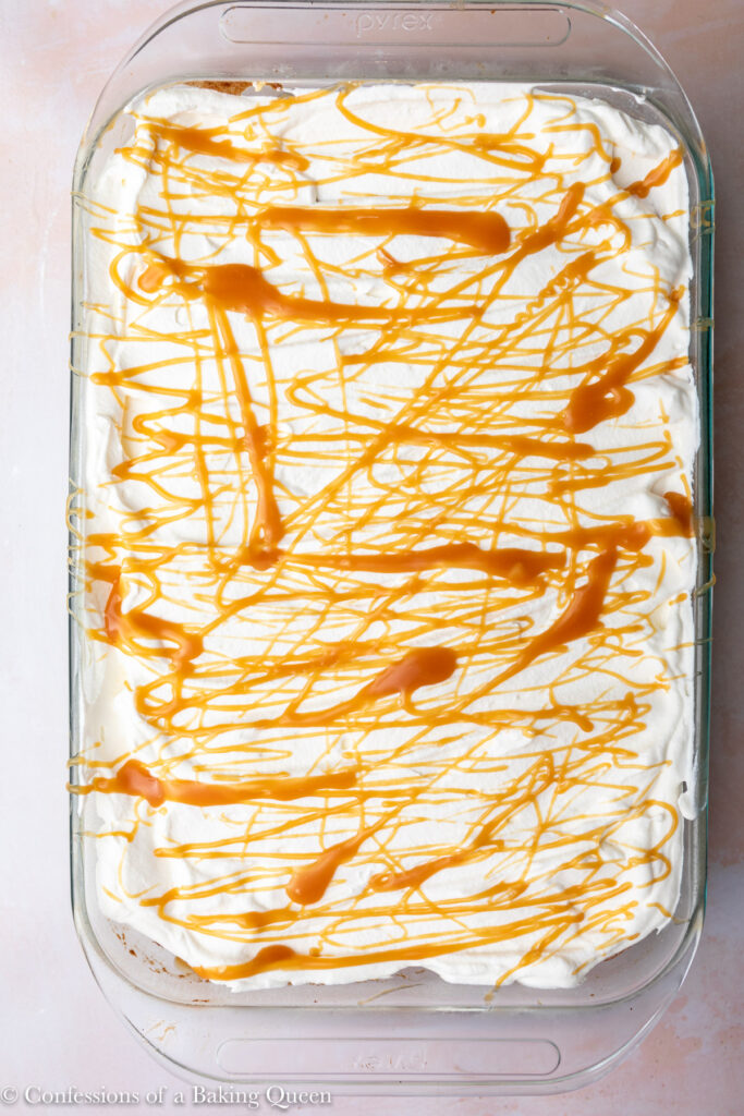 salted caramel drizzled on top of whipped cream on a tres leches cake in a glass dish on a light pink surface