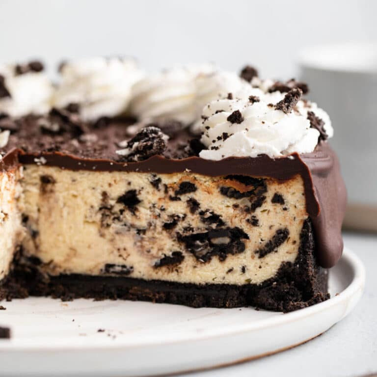 cut open oreo cheesecake on a white plate on a grey surface with a wood knife and blue coffee cup