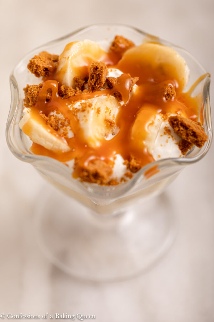 close up of deconstructed banana cream pie in a glass dish on a white marble surface