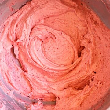 close up of strawberry cream cheese frosting in a metal mixing bowl on a light pink background