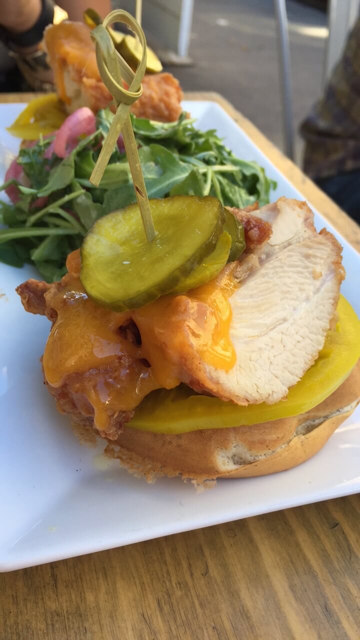 fried chicken sandwich with an argula salad on a white plate on a wood table