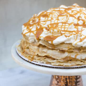salted caramel crepe caksalted caramel crepe cake on a cake stand on a marble background