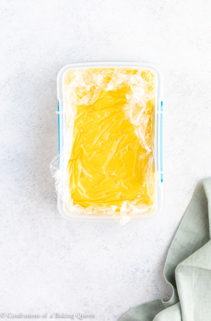 lemon curd cooling in a plastic container with plastic wrap on the top