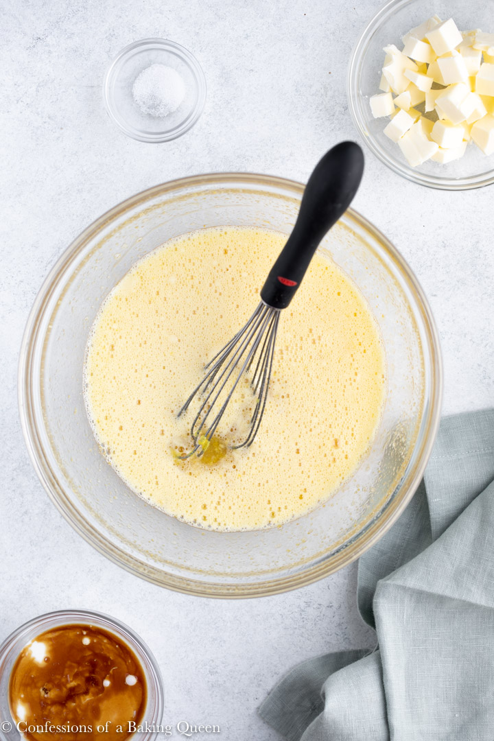 lemon curd recipe in a medium glass bowl with small bowls of butter, cream, salt and vanilla on the sides