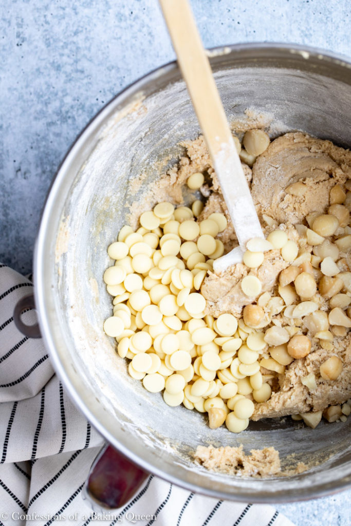 white chocolate and macadamia nuts added to cookie batter in a metal bowl