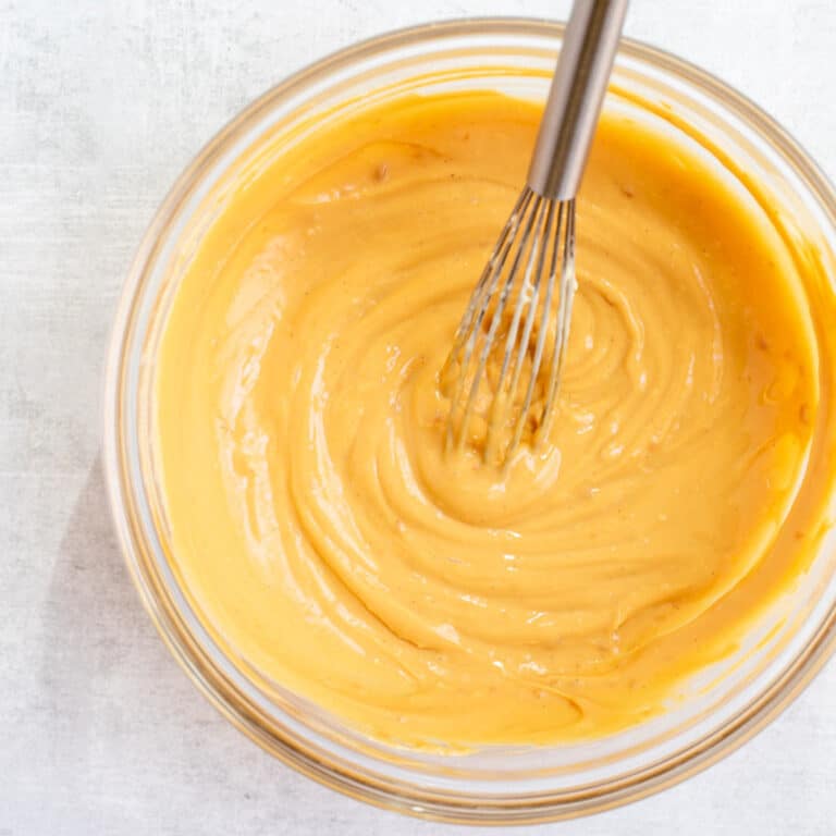 dulce de leche pastry cream in a glass bowl with a metal whisk on a grey background