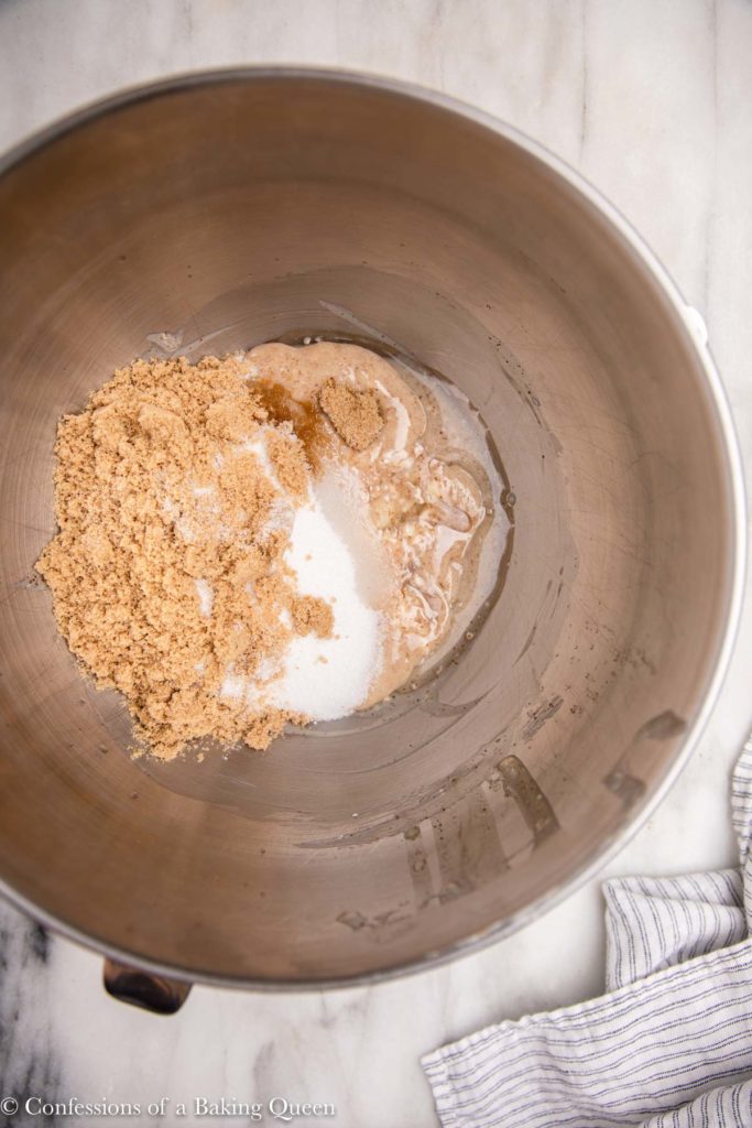 brown sugar, granulated sugar added to butter in a metal mixing bowl on a white marble surface with a white stripped linen 