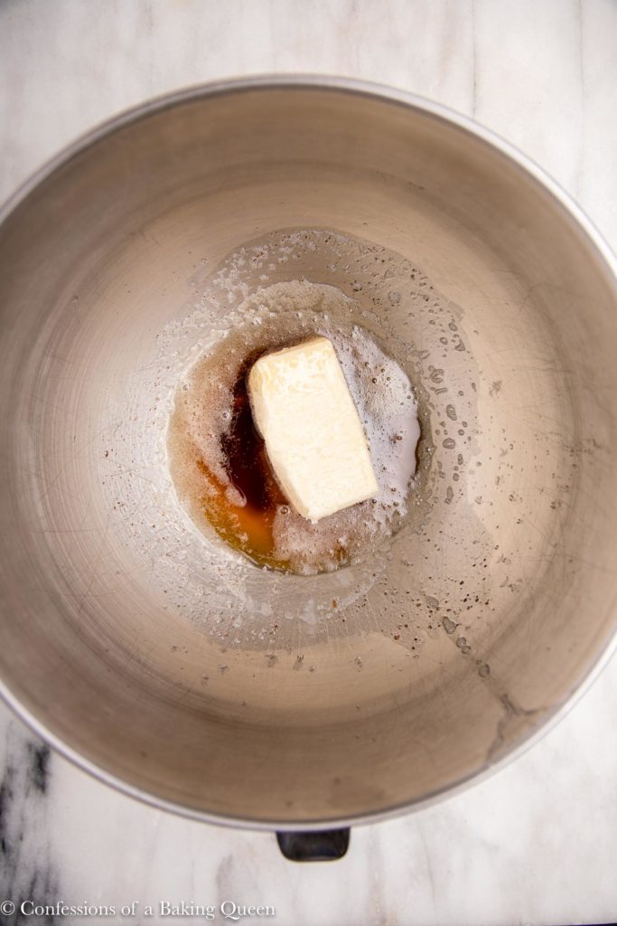 stick of butter added to a metal bowl with brown butter  on a white marble surface