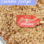 banana nut granola pressed down with an orange spatula on a metal baking pan before baking on a white surface