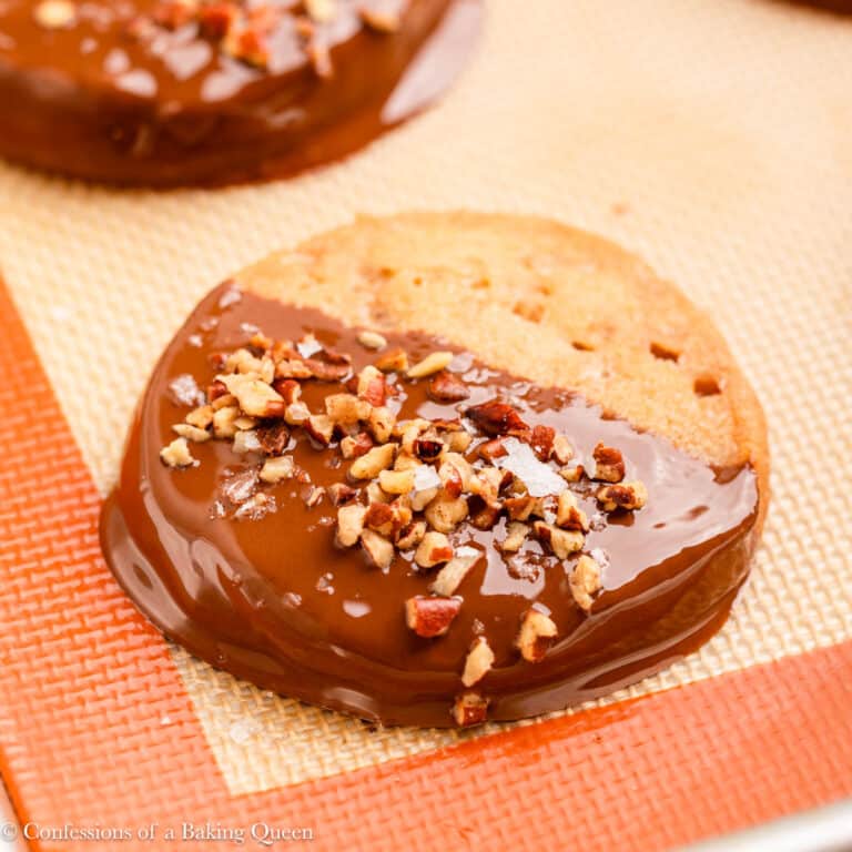 pecans and sea salt sprinkled on top of chocolate dipped brown butter cookie on a light surface.