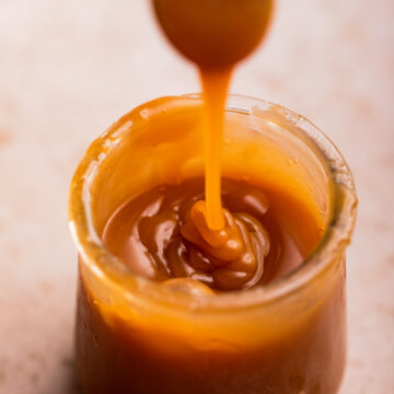 spoon dripping salted caramel sauce down into a glass pot on a light brown surface
