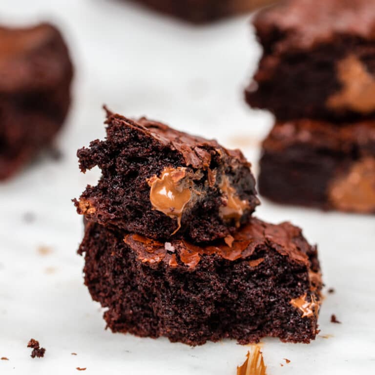 thick and chewy brownies baked and stacked on top of each other broken apart showing melted chocolate on a white marble background