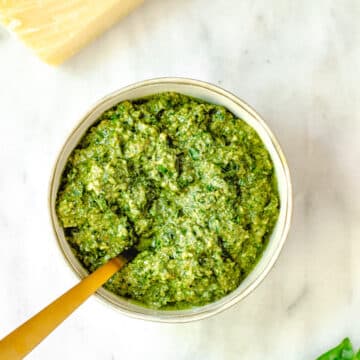 easy walnut pesto recipe served in a small bowl with a gold spoon on a white marble surface with a block of parmesan cheese and basil leaves